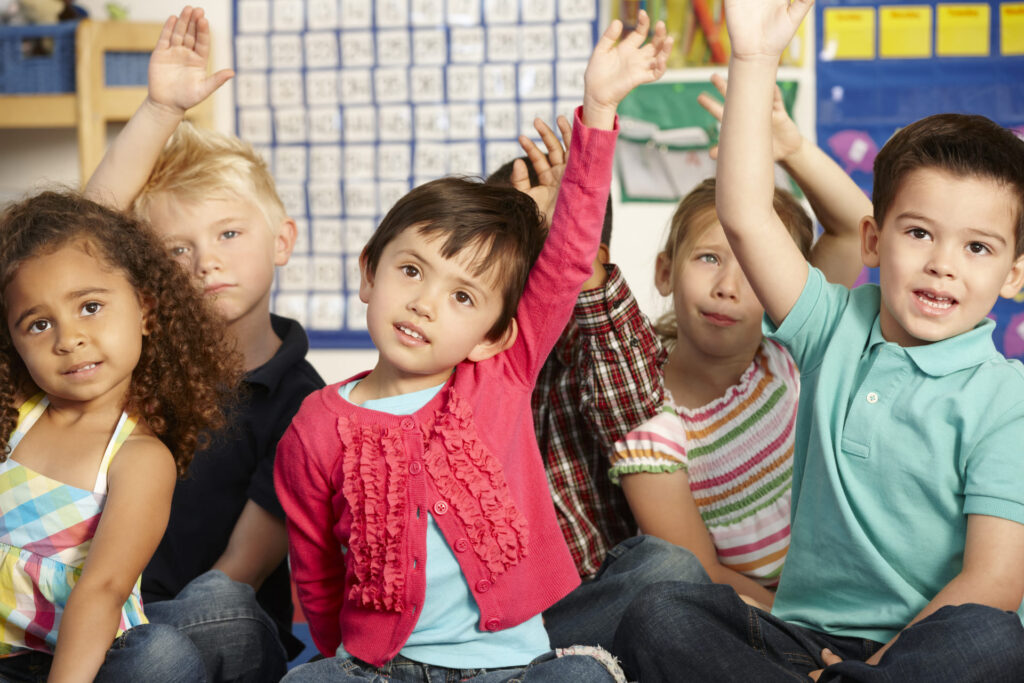 Diverse group of preschoolers raising their hands