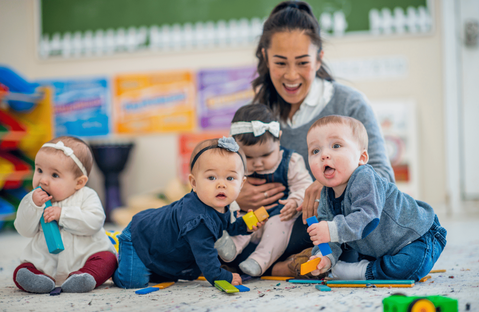 Infant teacher sitting with four babies in a child care room