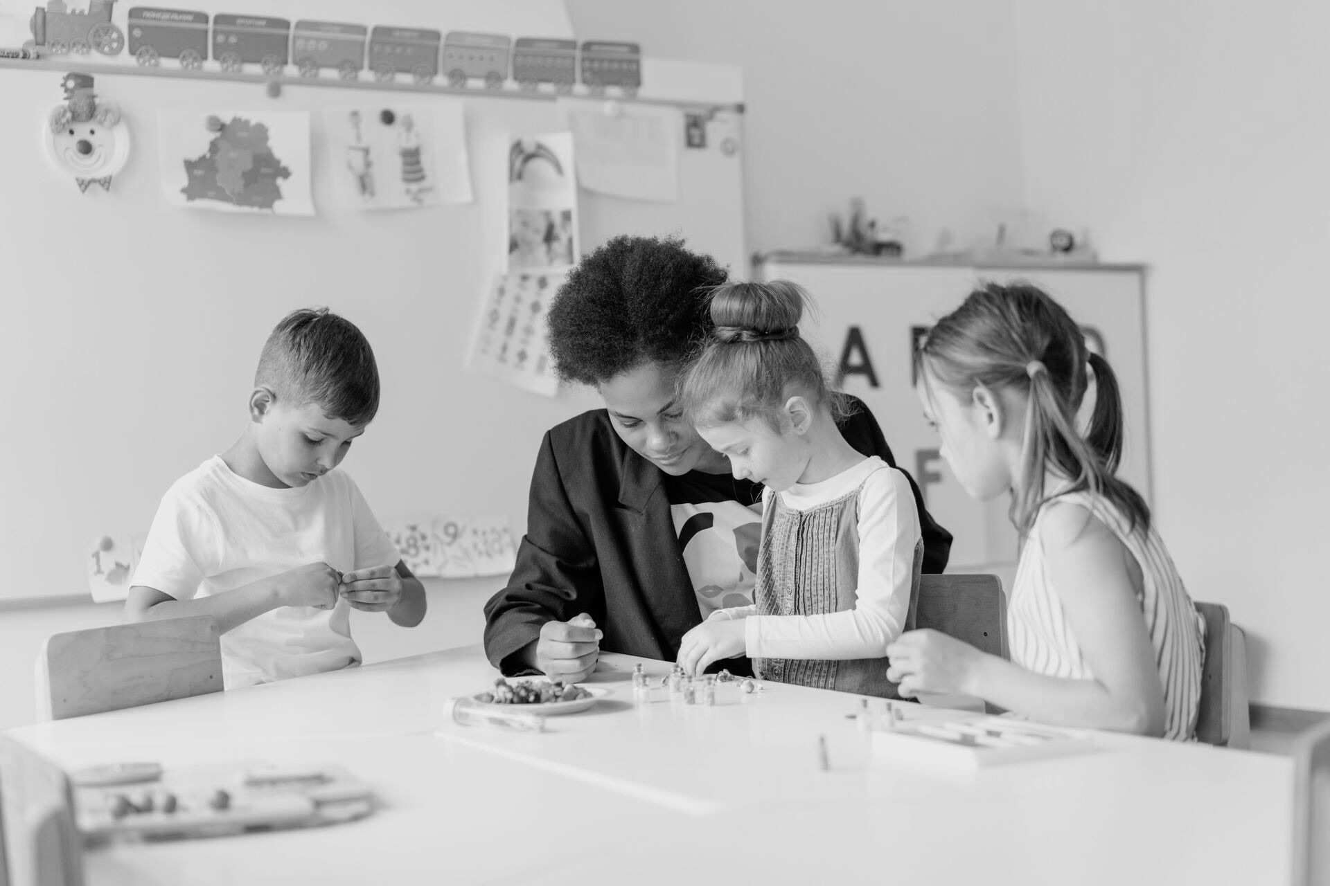 Teacher helping preschool children with an activity at a classroom table